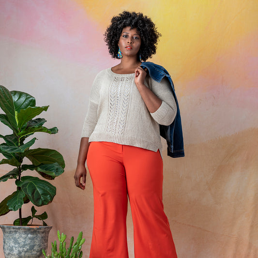 Front view of a plus size African American woman wearing Llana del Rio, a long sleeve scoop neck sweater with wide lace panel in the front, knit in Kelbourne Woolens Mojave in natural.