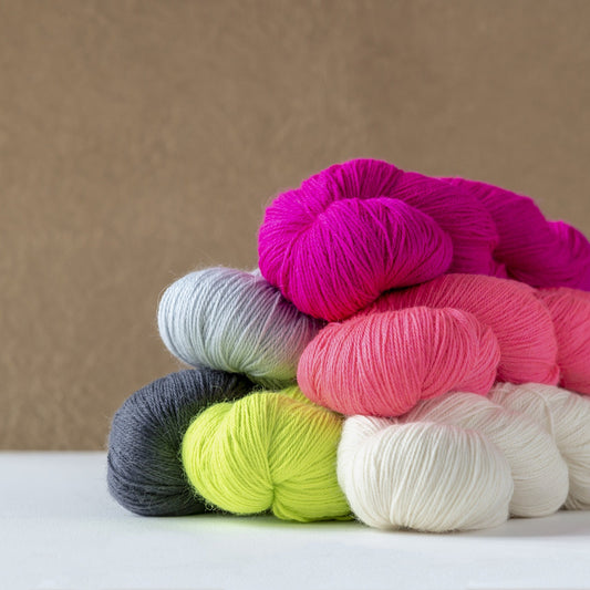 kelbourne woolens perennial yarn in skeins, piled on a table, against a tan background.