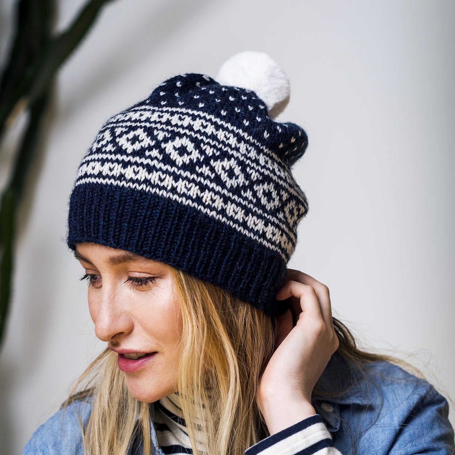 A Chinese American woman in a modern plant store wearing Ballard, a hand knit color work beanie in Kelbourne Woolens Scout in natural and navy heather.