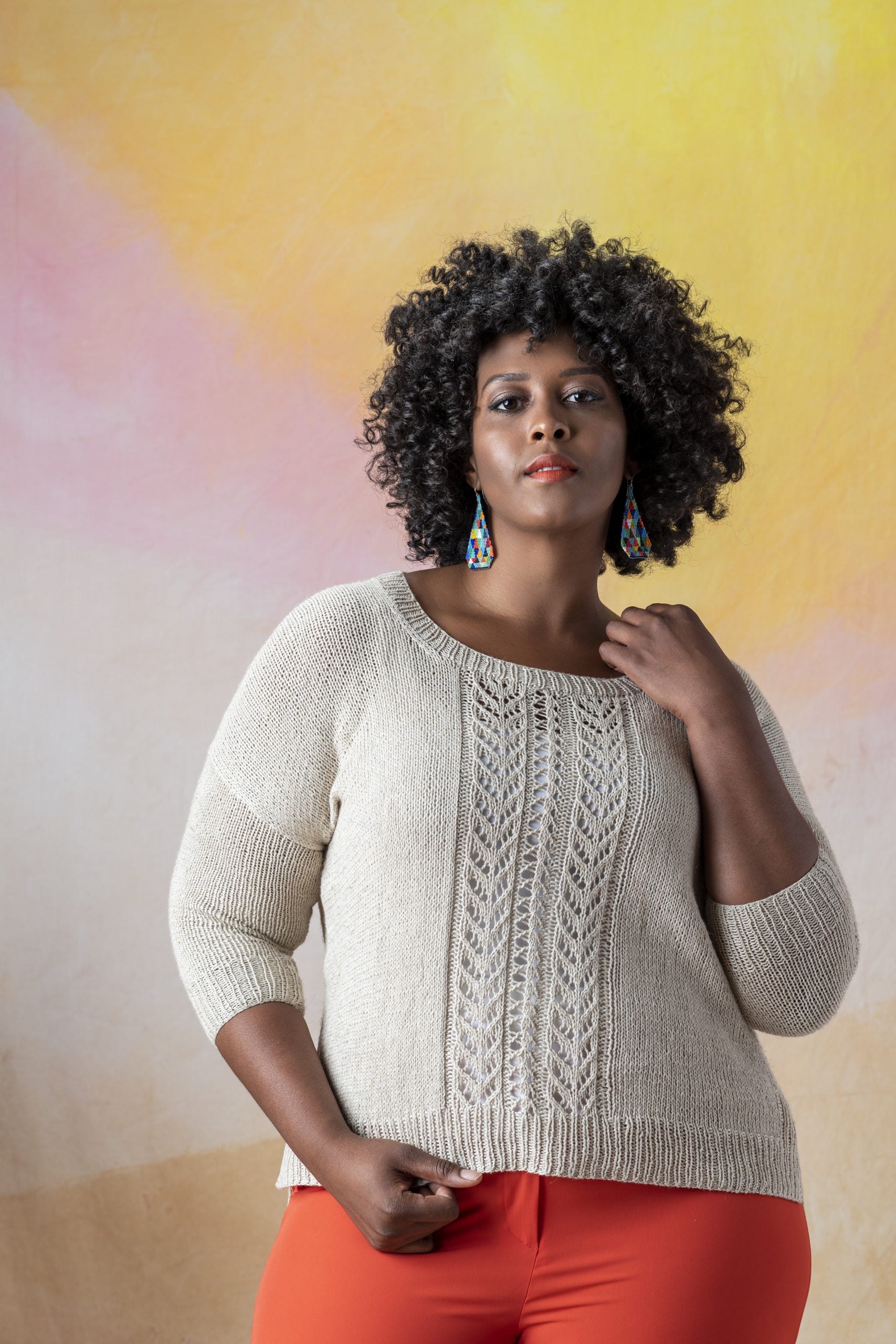 Front view of a plus size African American woman wearing Llana del Rio, a long sleeve scoop neck sweater with wide lace panel in the front, knit in Kelbourne Woolens Mojave in natural.
