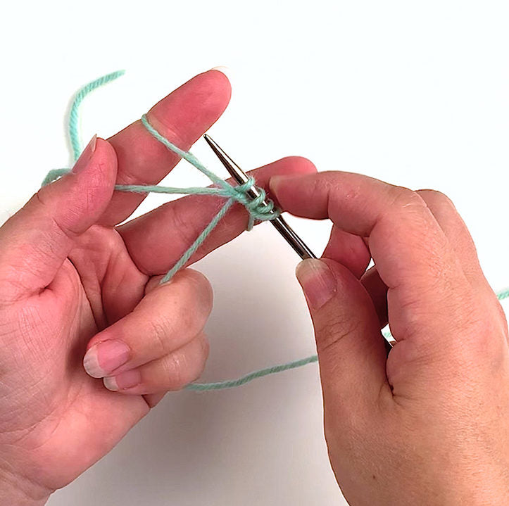 Two hands casting on a metal knitting needle with mint green yarn