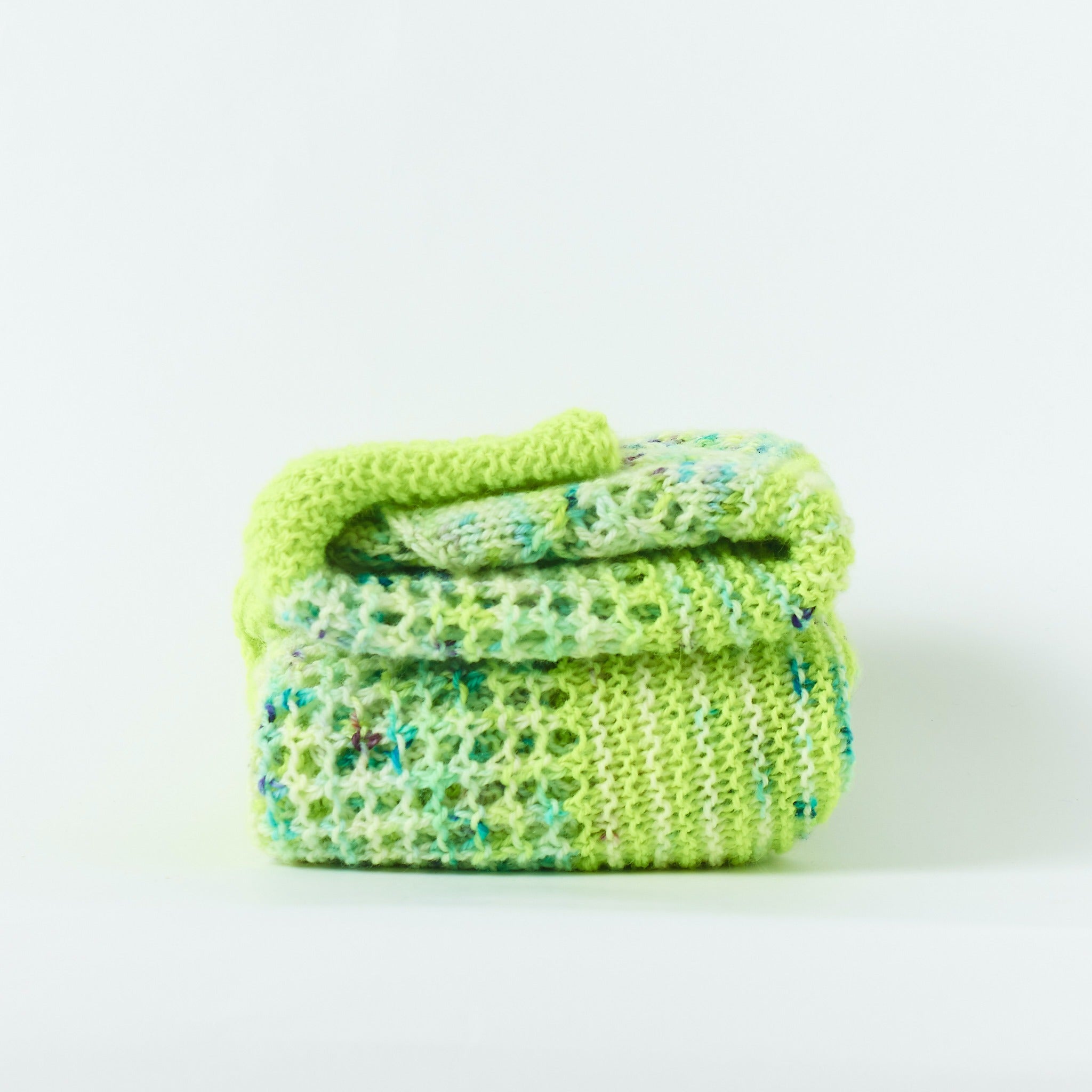 Handknit shawl folded neatly in a square knit out of neon lime and blue speckled yarn
