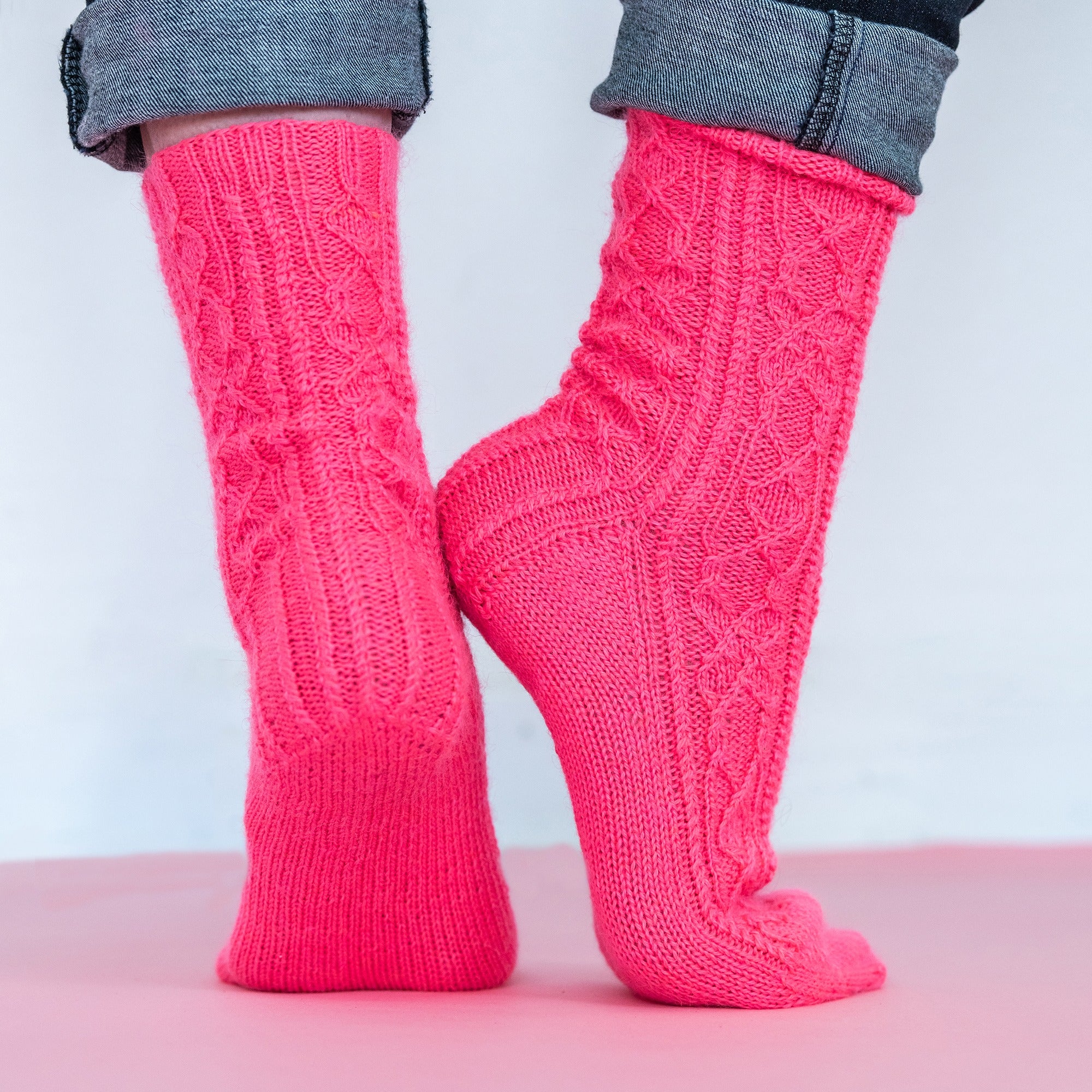 Close up shot of the lower legs and heels of a model wearing the Sweet Pea Socks by Jennifer Burke in Kelbourne Woolens Perennial in neon coral.